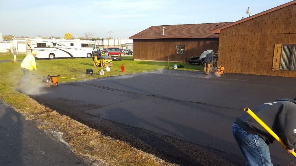 A man is using a shovel to spread asphalt on a driveway