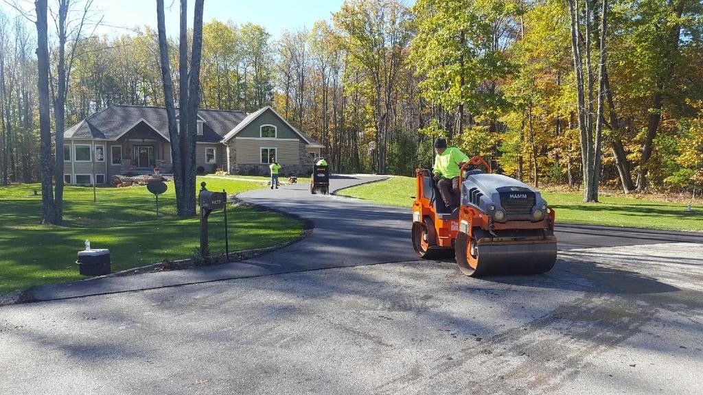 A man is driving a roller down a driveway in front of a house.