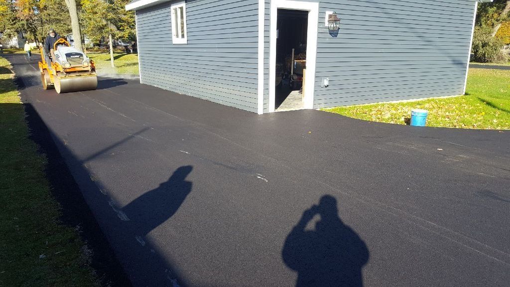 A man is taking a picture of a driveway in front of a house.