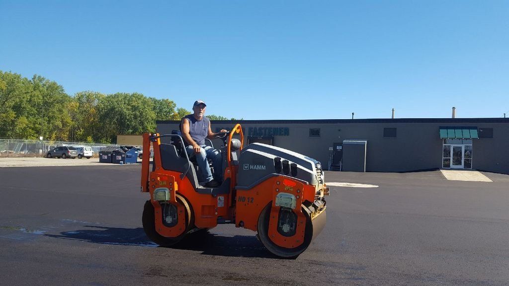 A man is driving a roller in a parking lot.