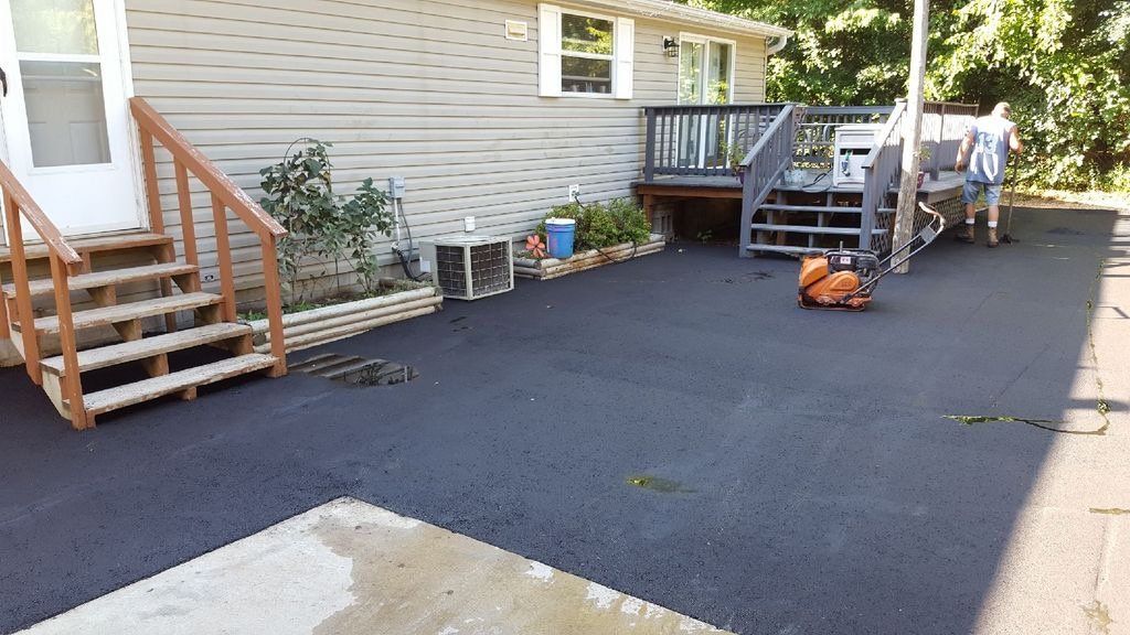 A house with stairs and a black driveway in front of it.