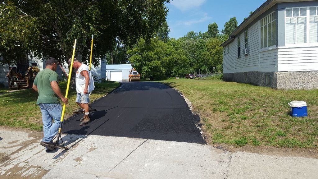 Two men are working on a driveway in front of a house