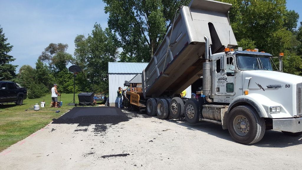 A dump truck is being loaded with asphalt in a driveway.
