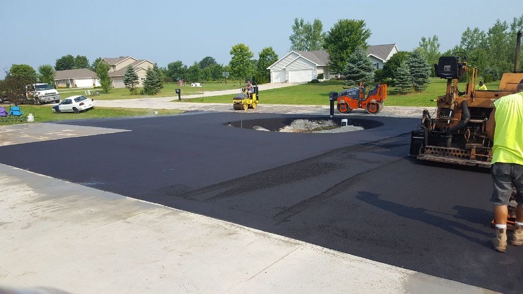 A man in a yellow vest is walking across a asphalt driveway