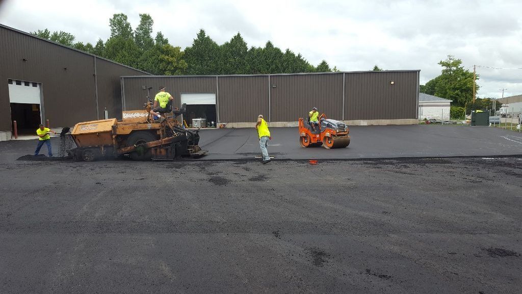 A group of construction workers are laying asphalt in a parking lot