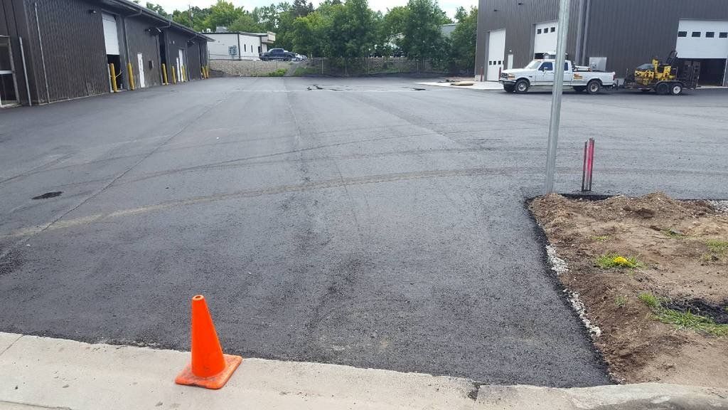 An orange cone sits on the sidewalk in front of a parking lot