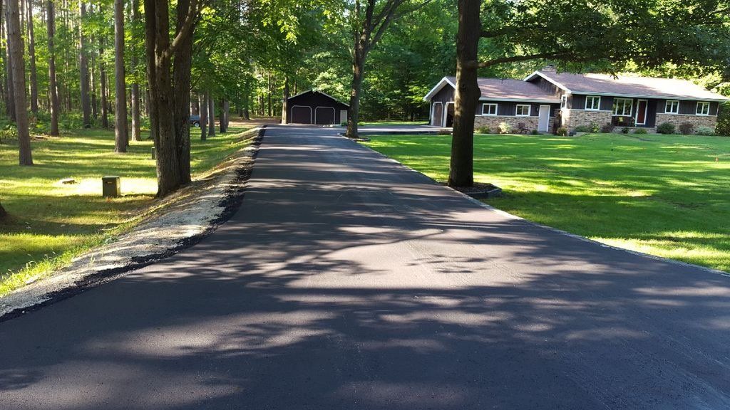 A driveway leading to a house surrounded by trees and grass.