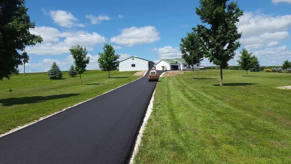 A car is driving down a road next to a grassy field.