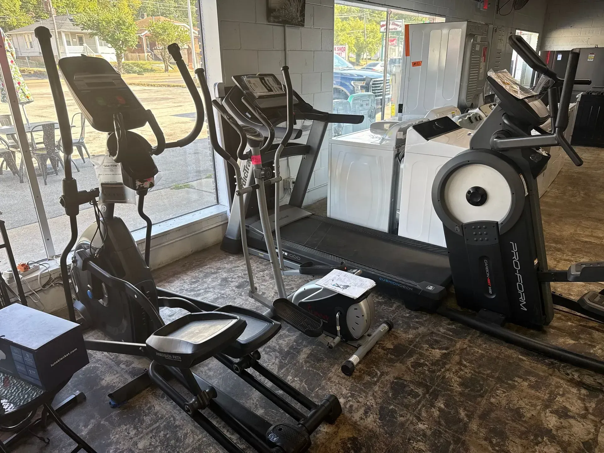 A showroom with elliptical machines, a treadmill, and other exercise equipment displayed near a window.