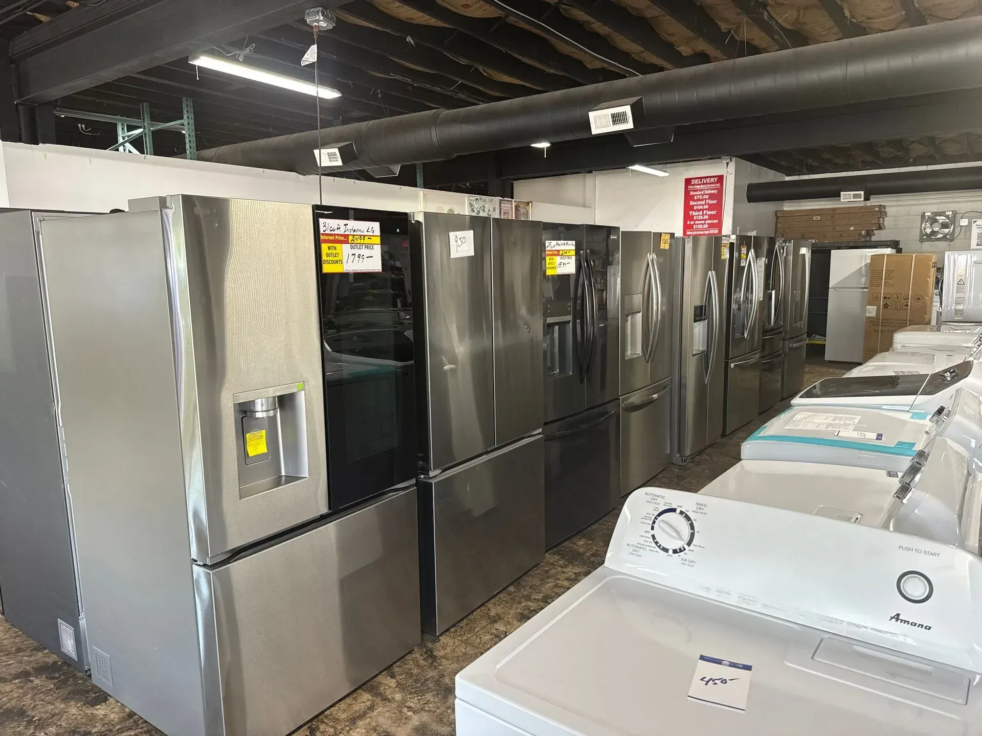 Refrigerators and washing machines for sale in a store. Stainless steel appliances on display.