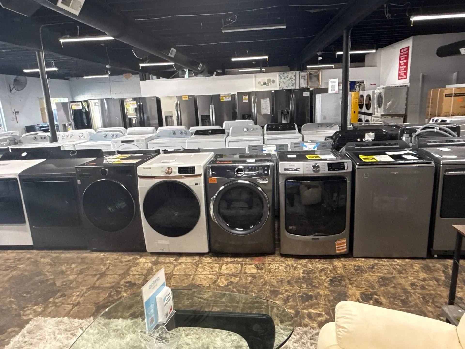 Appliances for sale in a store: washing machines and dryers in various colors.