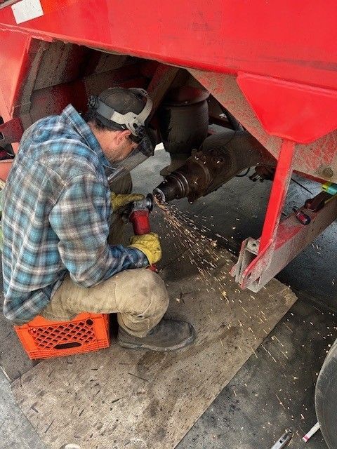 Person welding under a red vehicle, with sparks flying in a workshop garage