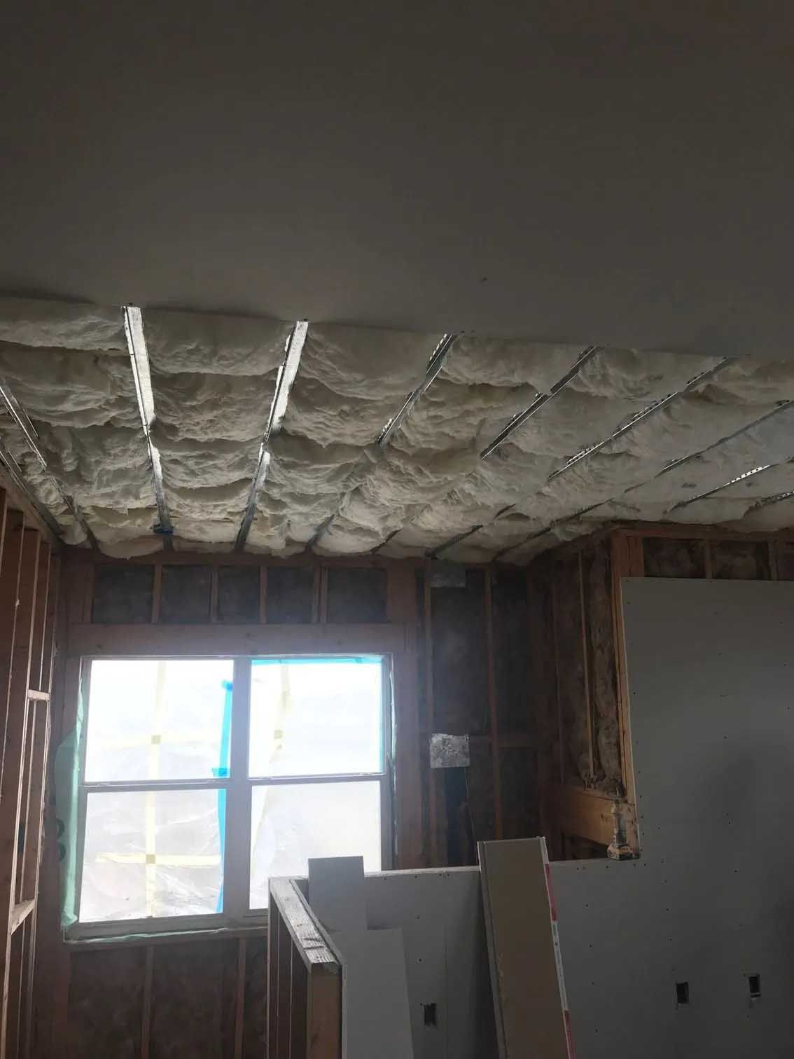 Interior view of a room under construction with exposed wood framing, insulation in the ceiling, and a window.