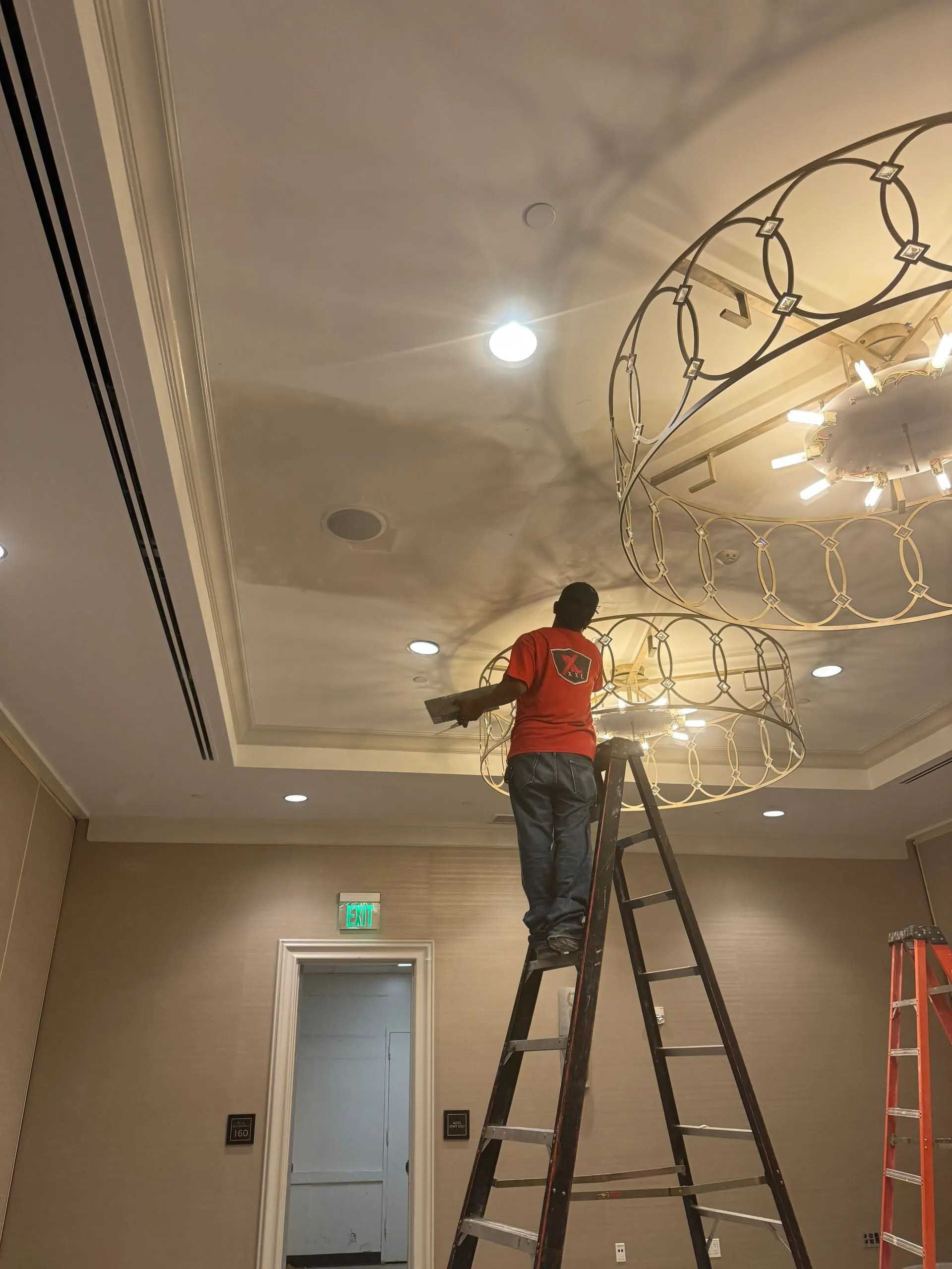 Person on a ladder installing lights on a decorative ceiling fixture in a room with a door.