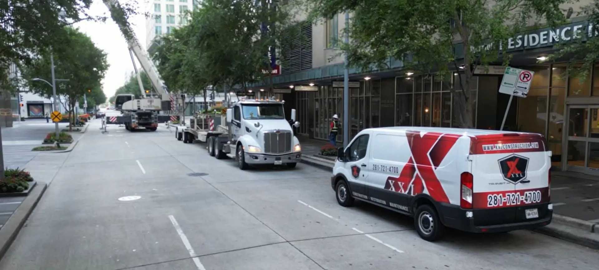 A city street scene with trucks and a van. A crane and construction are present near a building.