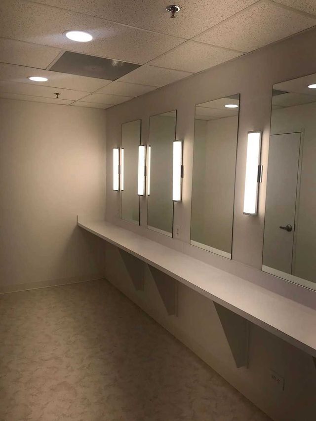 Empty dressing room with mirrors, lights, long countertop, and beige carpet.