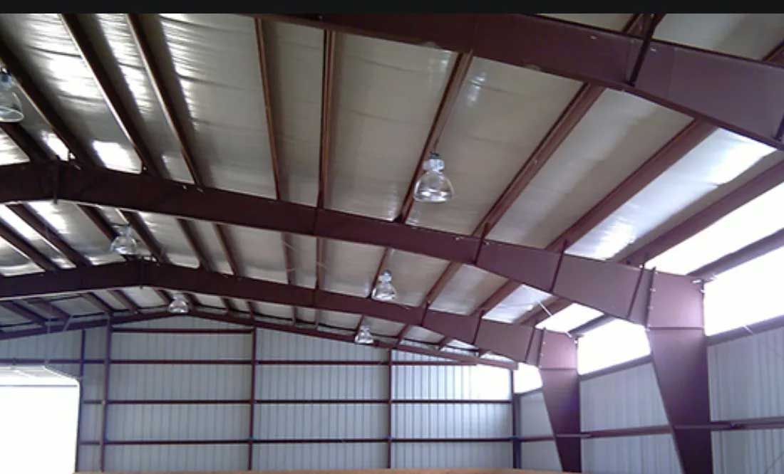 Metal framed building interior, burgundy beams, corrugated metal walls and ceiling, interior lights.