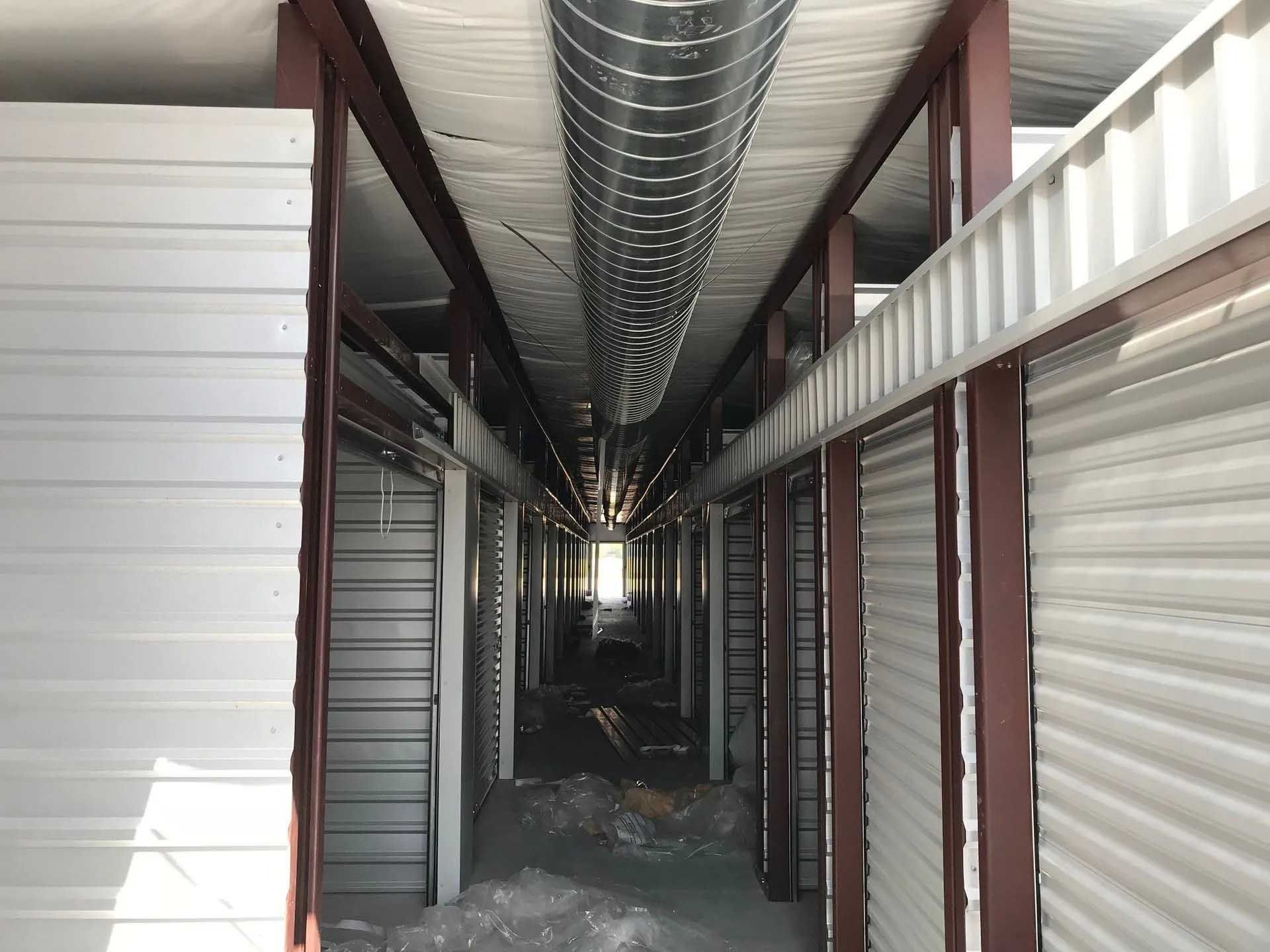 Interior view of a storage facility hallway, featuring storage units with rolling doors and a metal duct overhead.