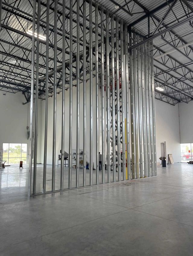 Interior view of a large room under construction; metal stud framework for a wall is visible, concrete floor.
