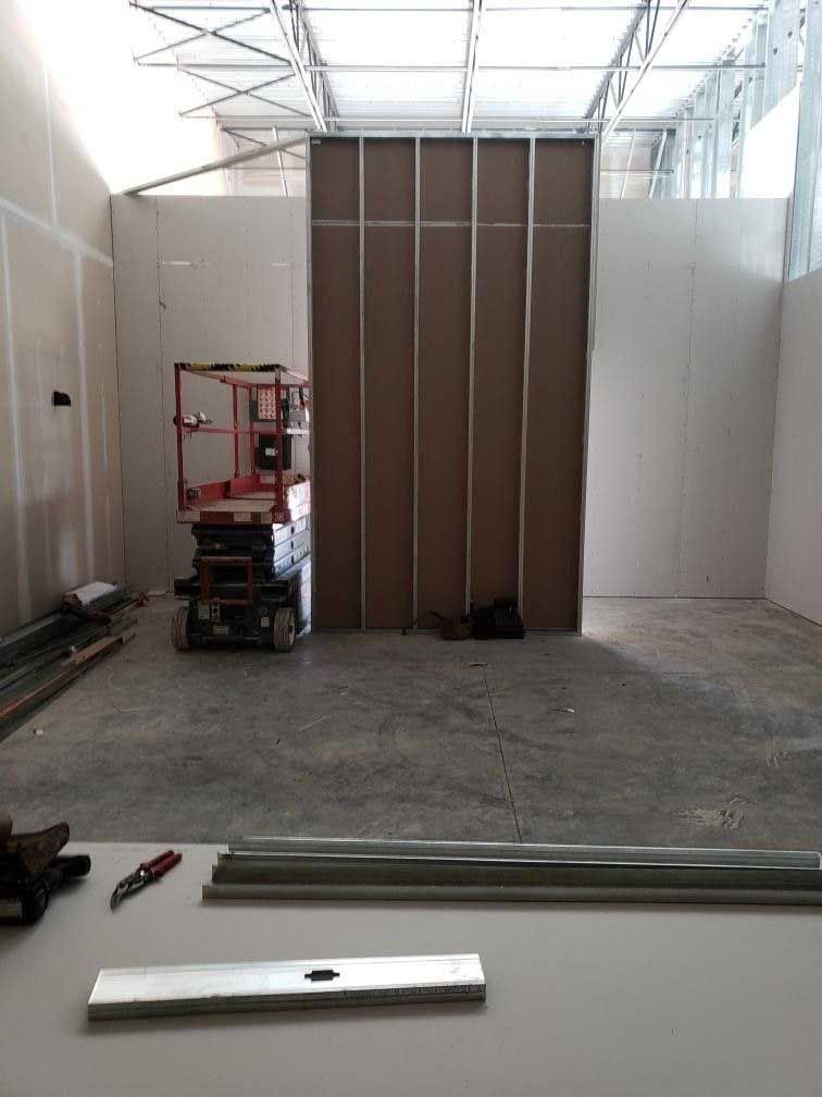Construction site: Interior with drywall, metal studs, lift, and materials.