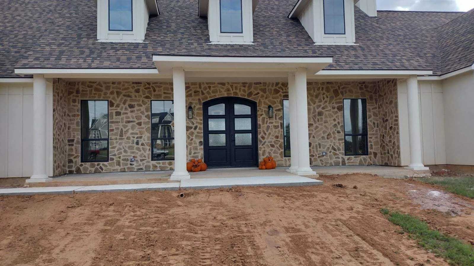 House exterior with stone facade, columns, dark door, and brown roof.