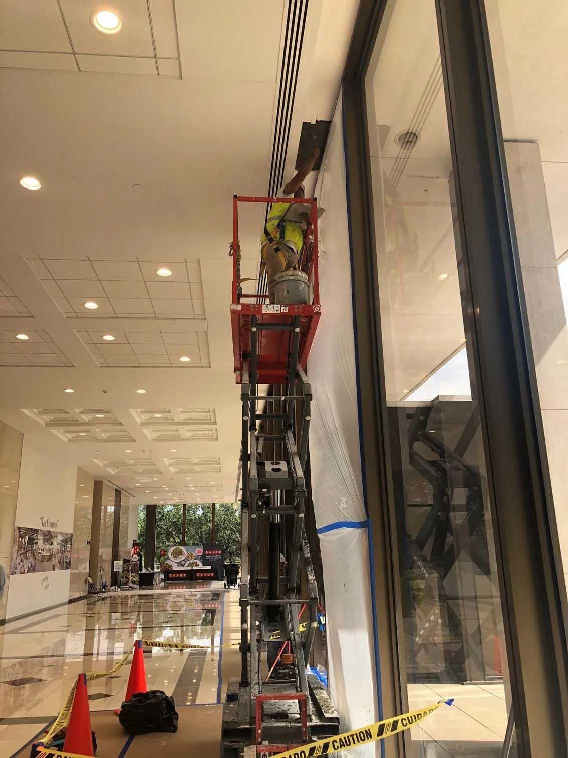 Person on scissor lift working on wall near large glass window.