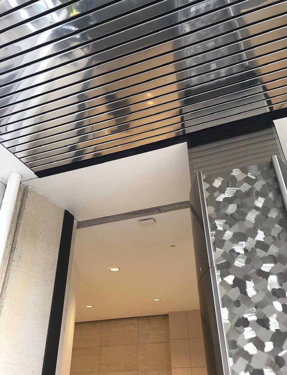 Interior architectural view: metal ceiling with black beams, white walls, and a patterned metal surface.