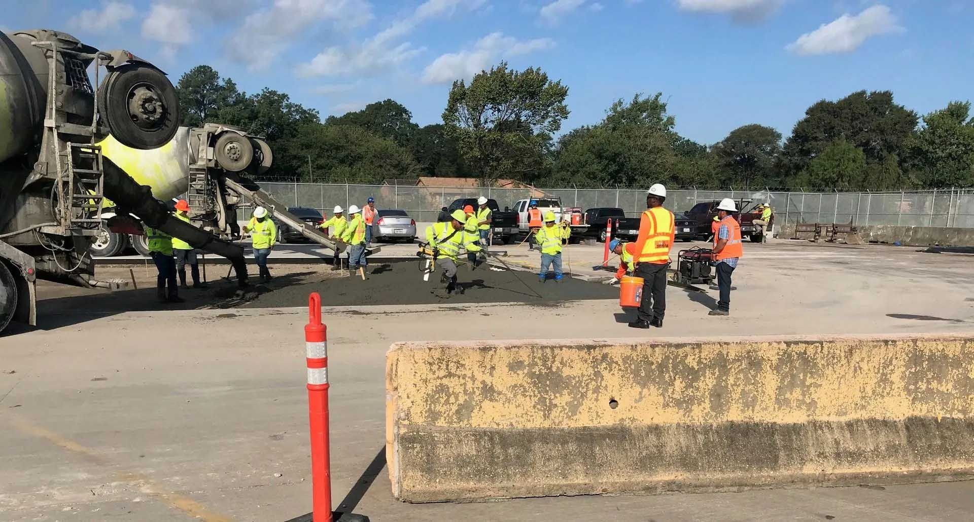 Construction workers in vests pour concrete from a truck on a roadway.