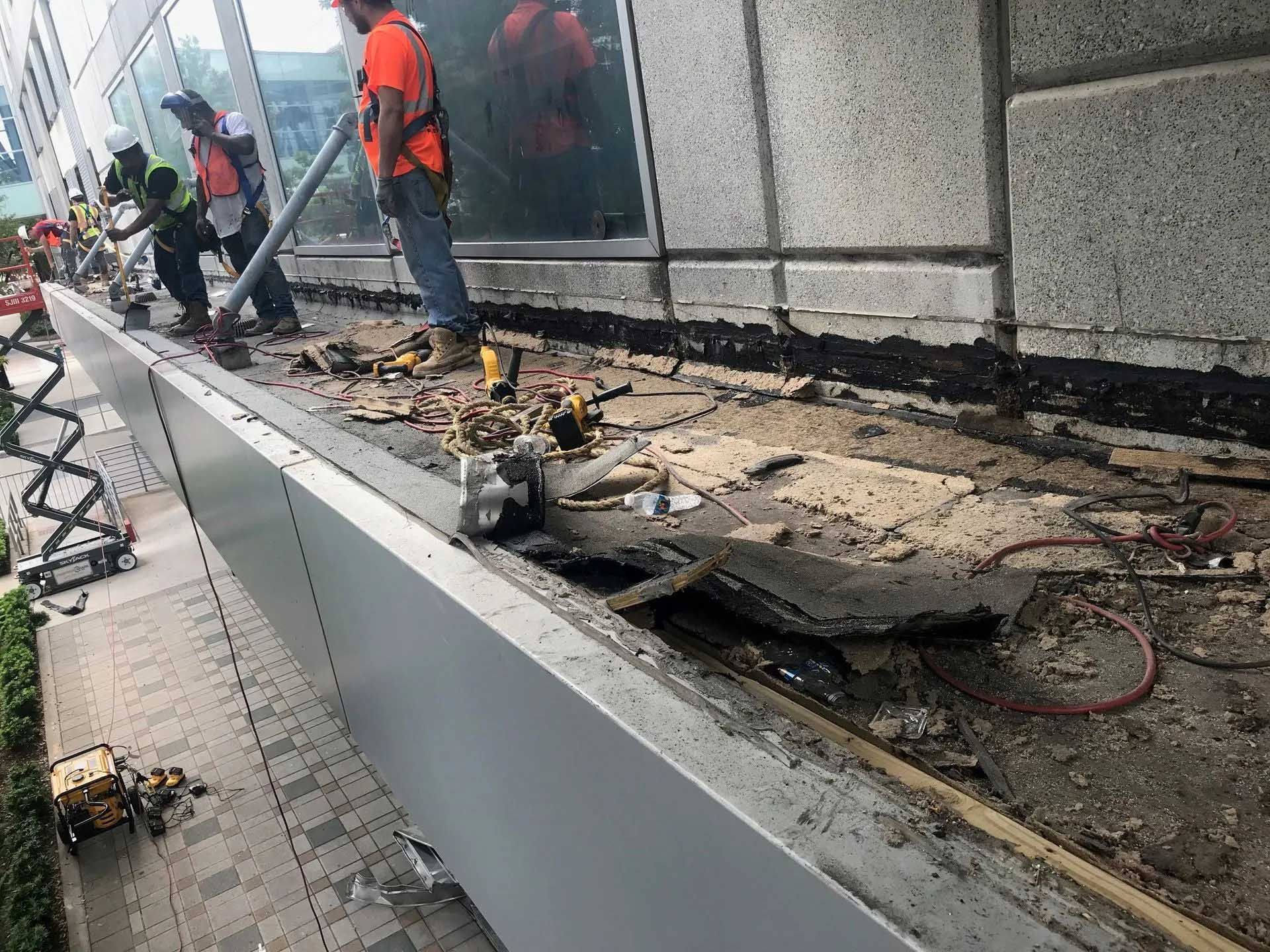 Construction workers repairing exterior building facade, using tools on a damaged ledge.