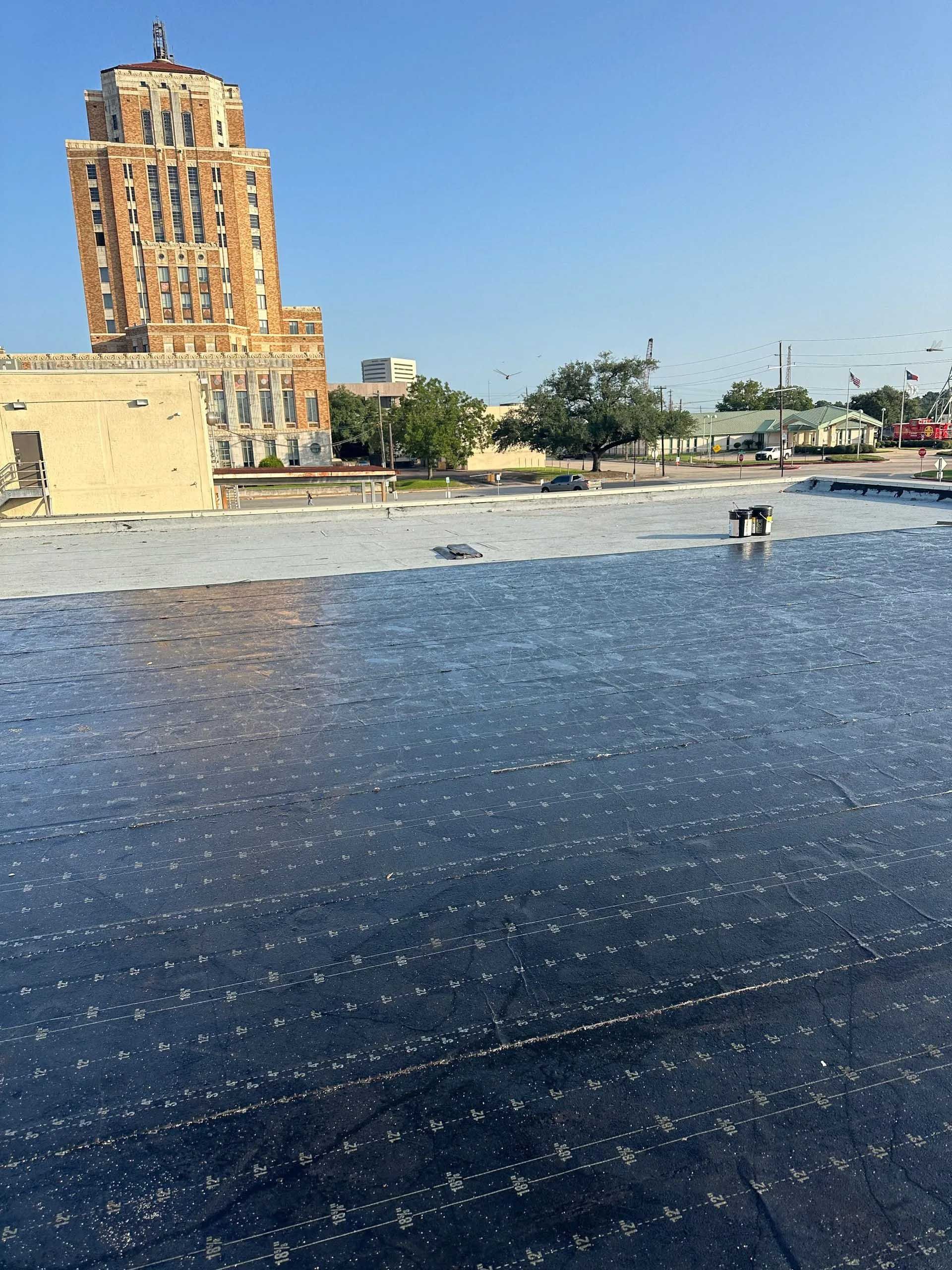 Rooftop with a dark, wet surface, two figures, and a tall, ornate brick building under a clear blue sky.