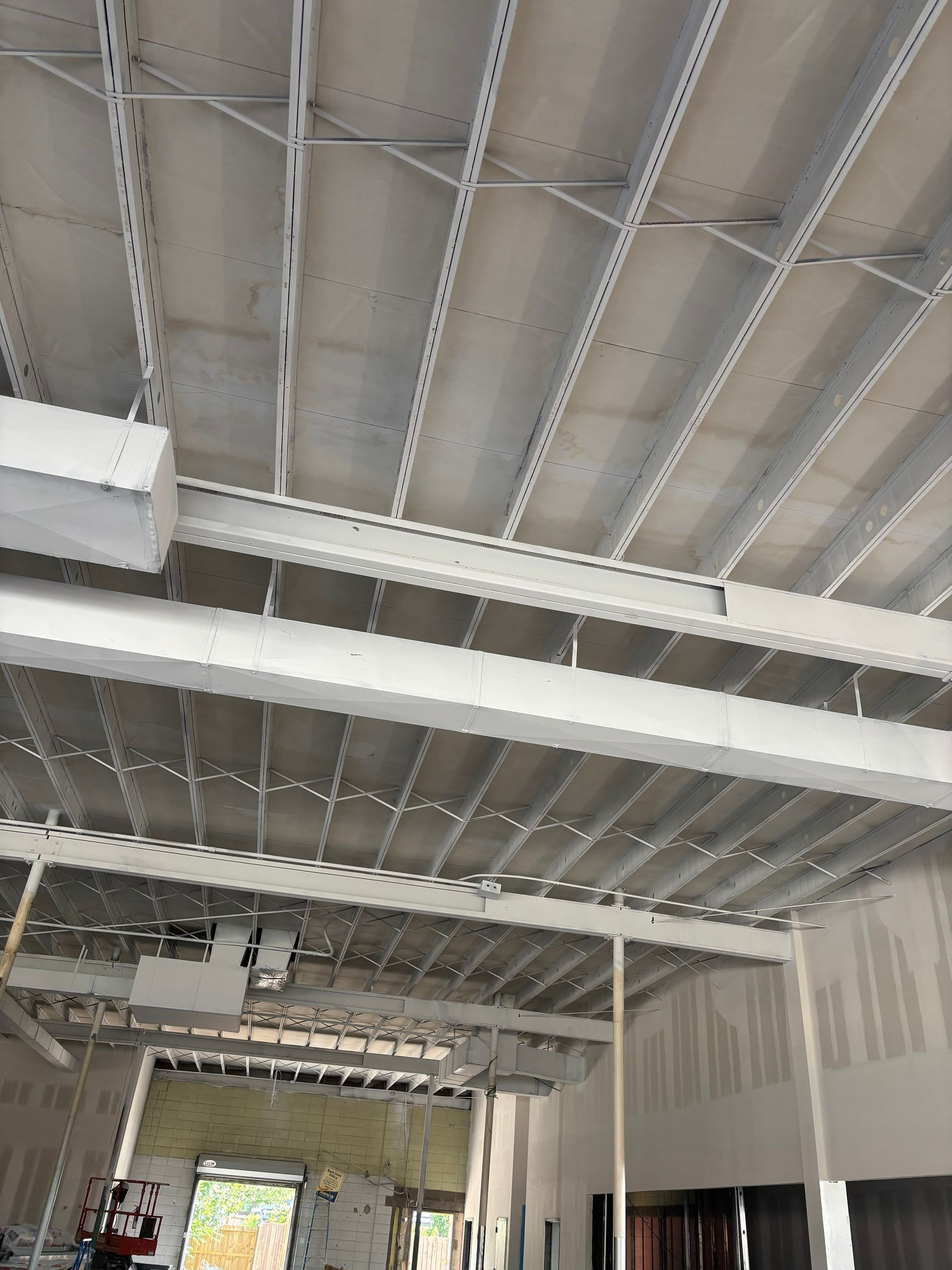 Construction site interior: Steel beams and concrete panels forming a ceiling, unfinished walls.
