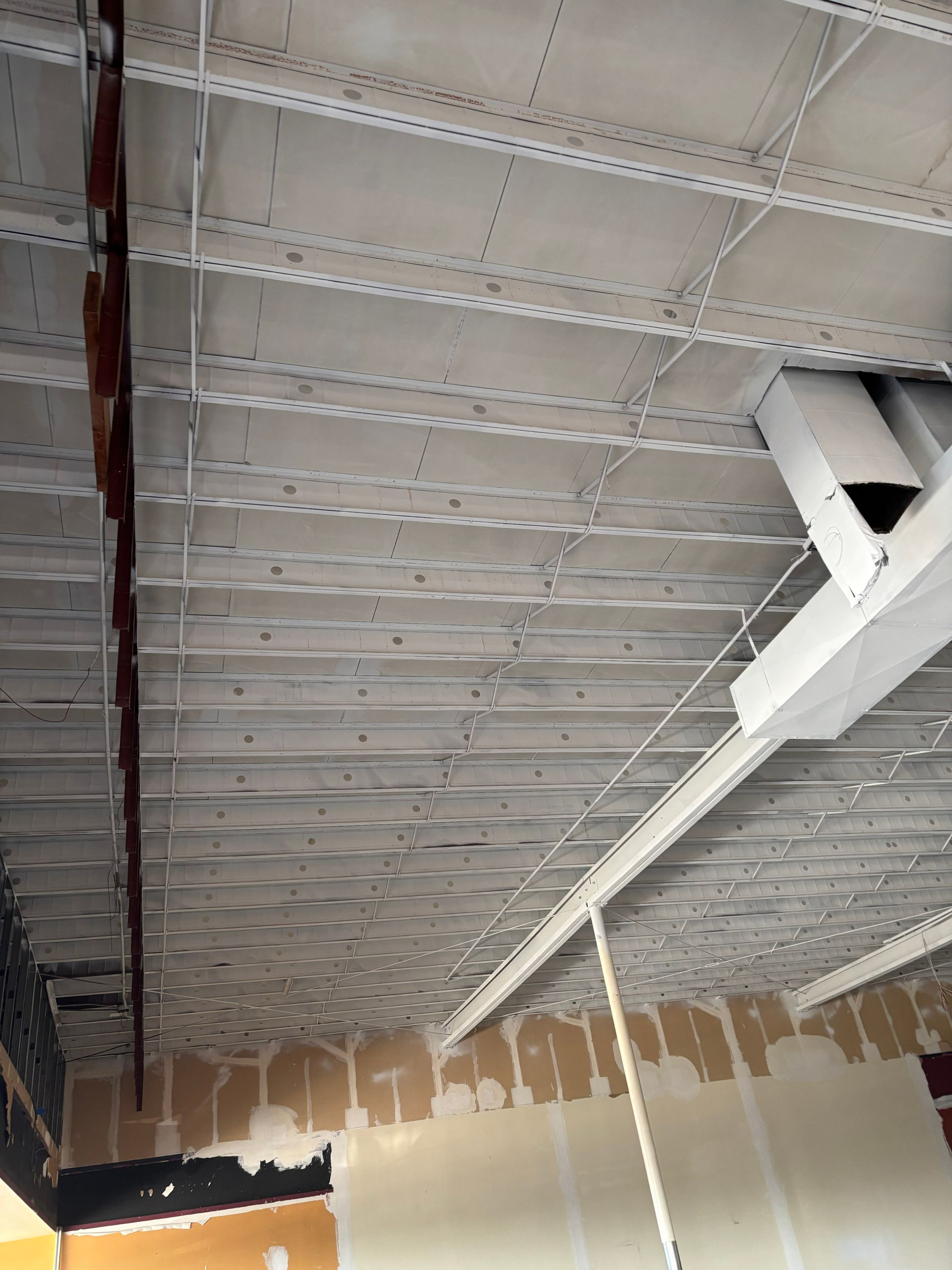 Gray concrete ceiling with metal supports and exposed wiring in a room with partially finished walls.