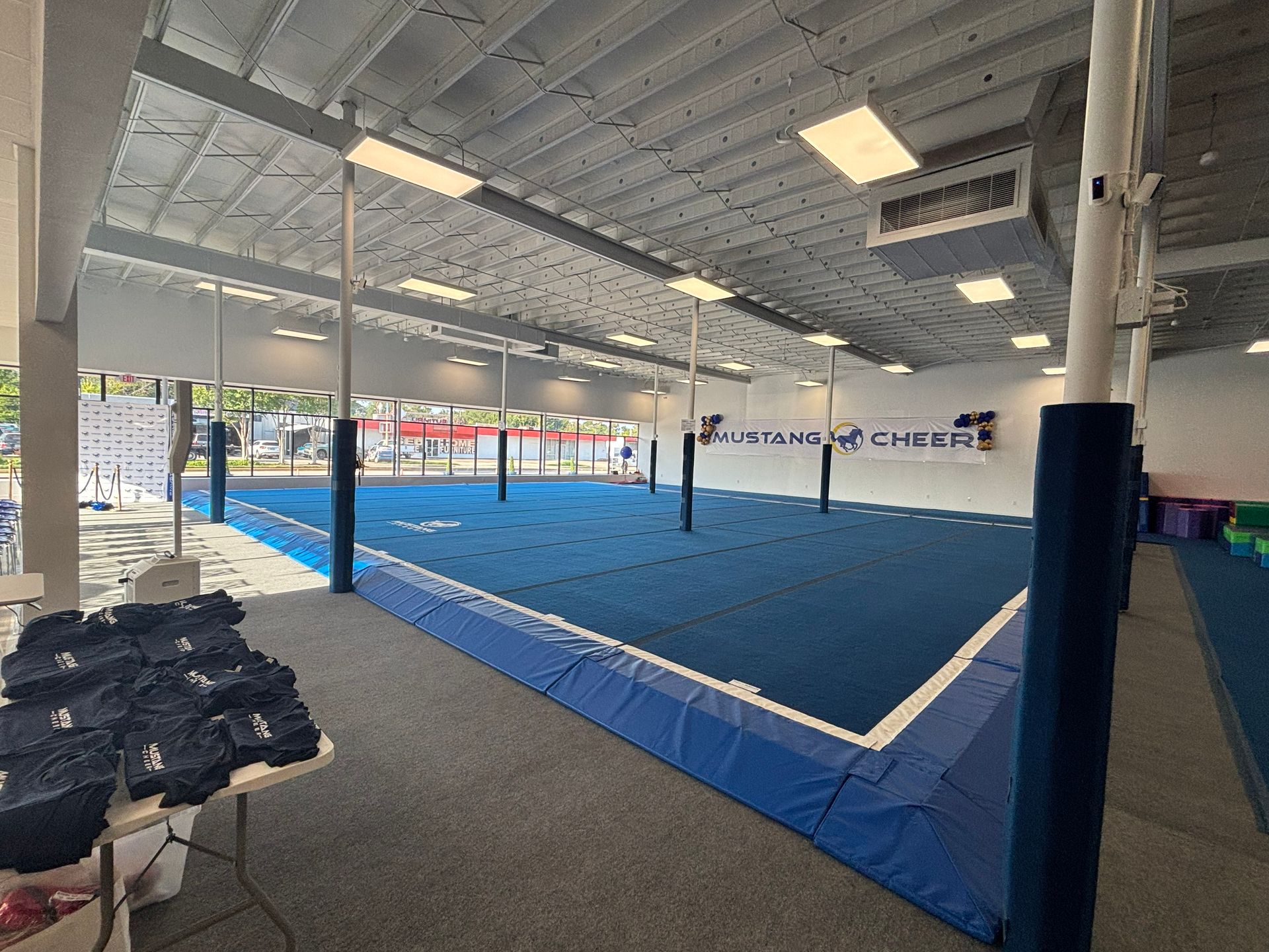 Indoor cheerleading training facility with blue floor and supportive poles.