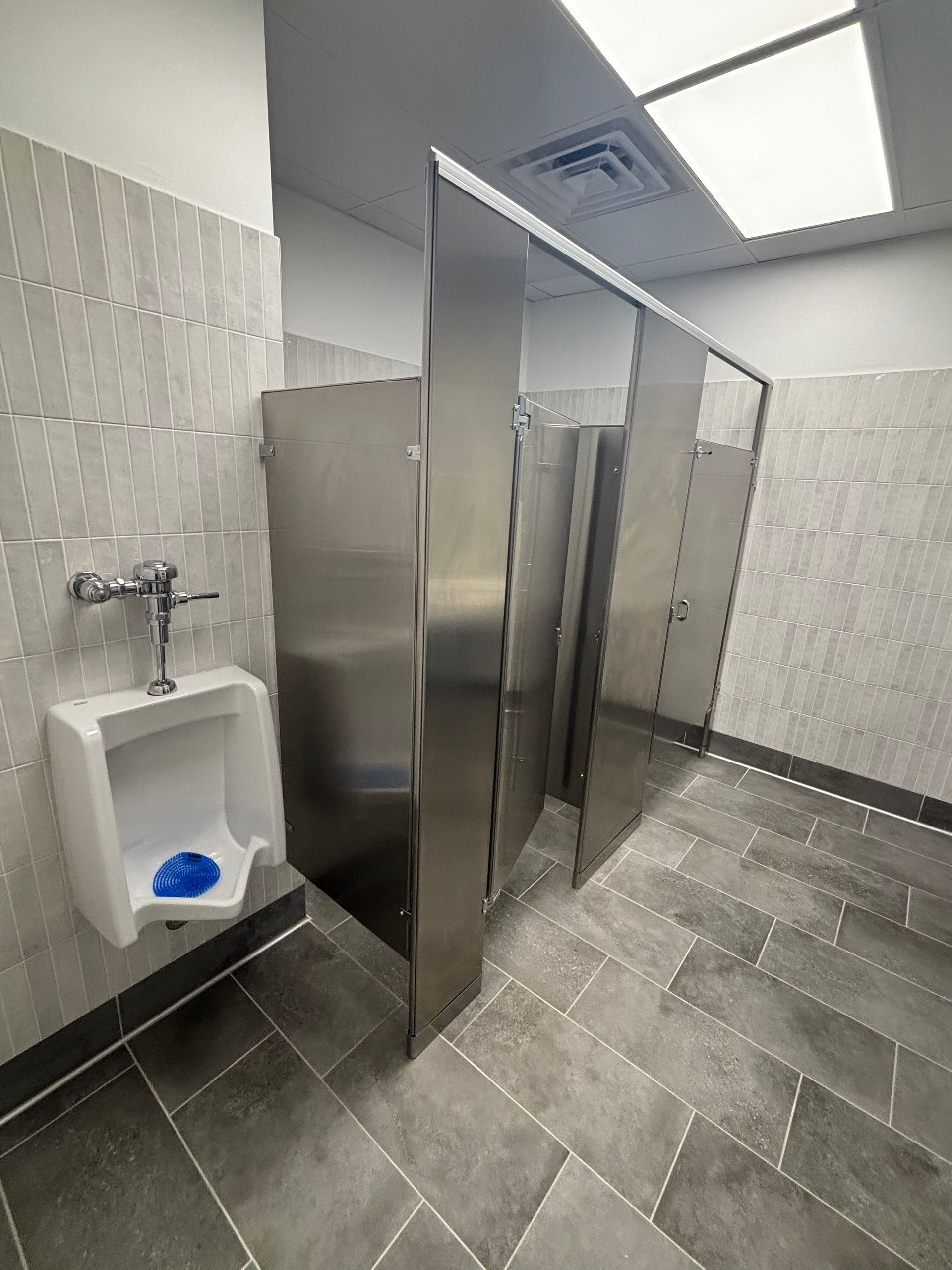 Public restroom with a urinal and stainless steel stall dividers.