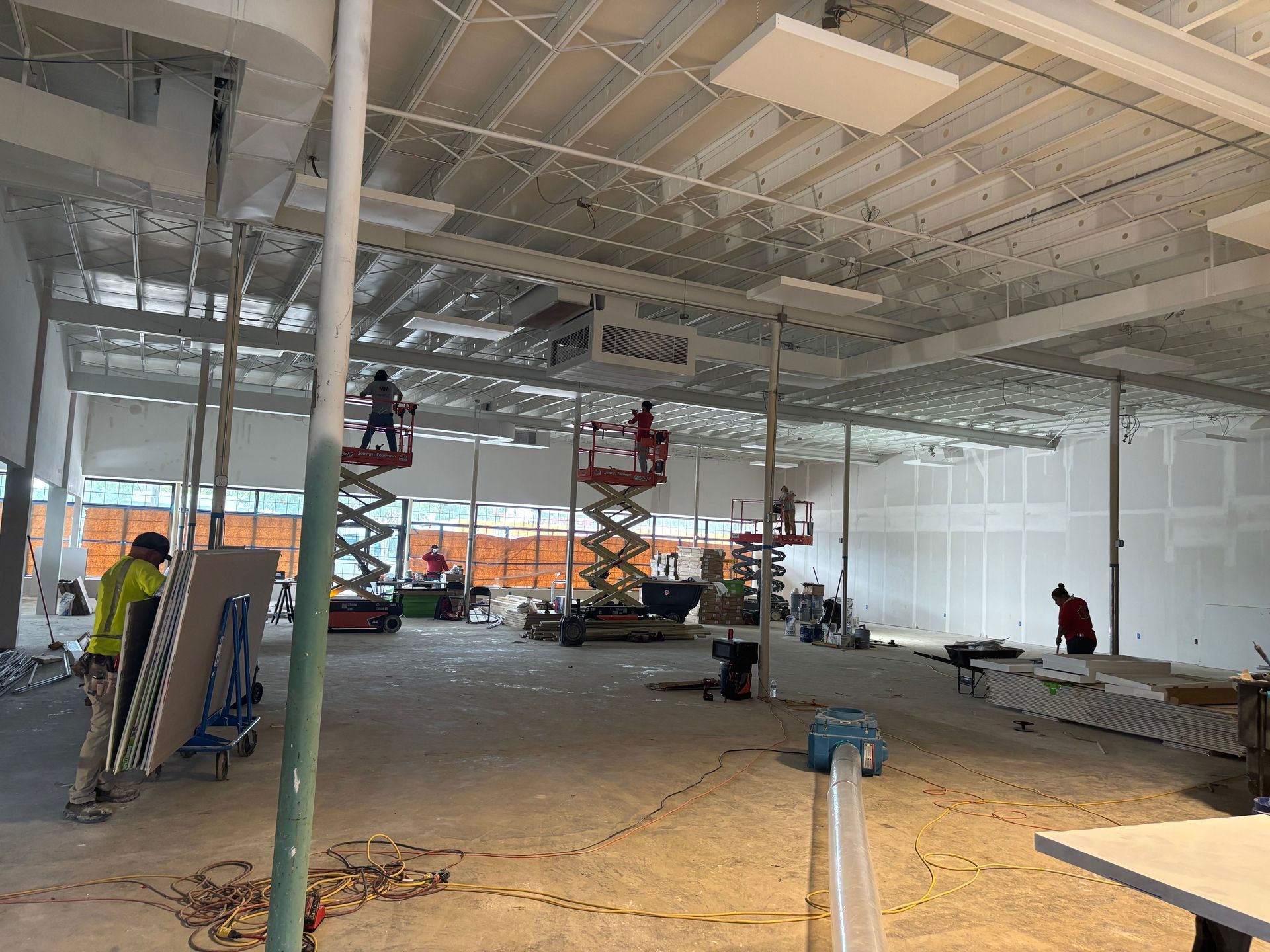 Interior of a construction site with workers on lifts and scaffolding; unfinished walls and ceiling.