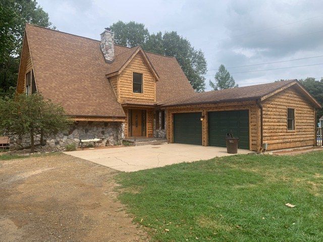 A log cabin with a garage and a driveway in front of it.