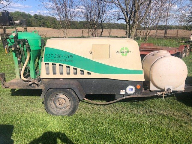 A sand blaster is parked in a grassy field.