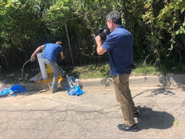 A man is standing on the side of the road taking a picture of another man.