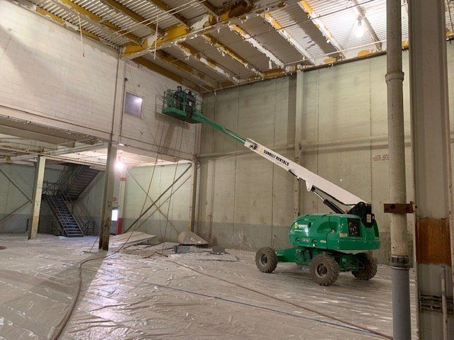 A green crane is sitting in the middle of a large warehouse.