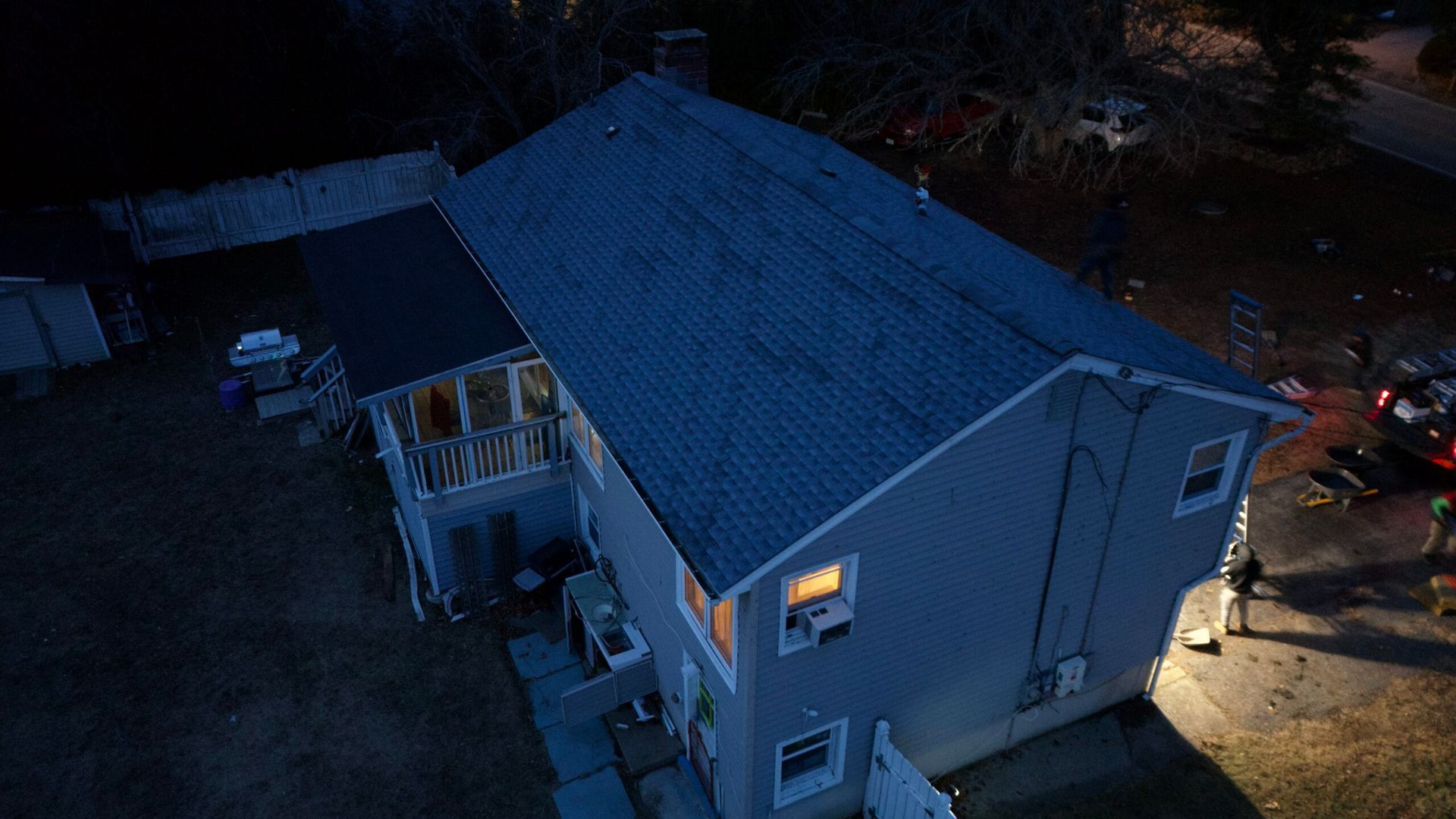 Aerial view of a small blue house at dusk with lit windows and porch lights.