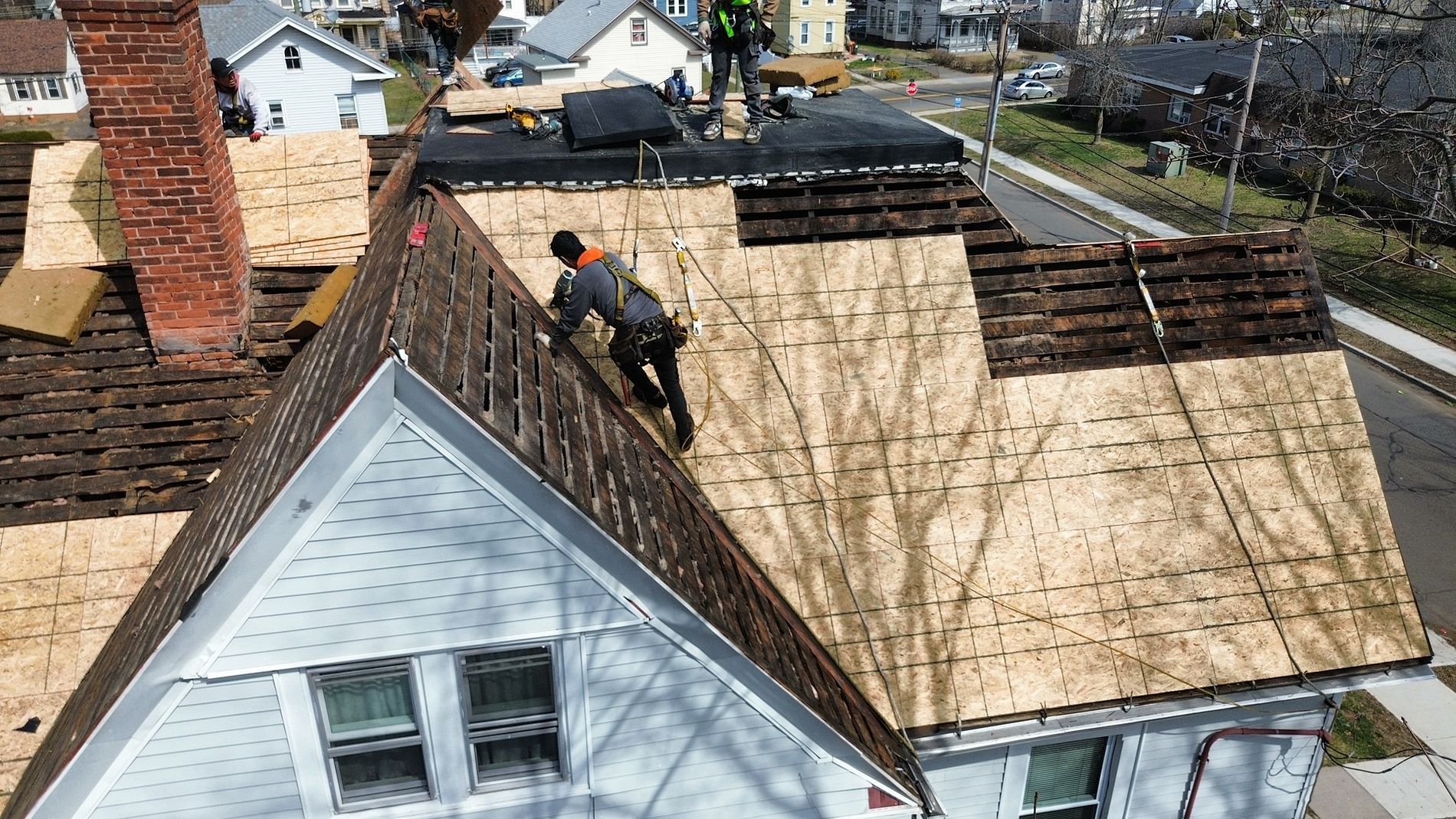 Worker repairing roof on a house beside another roof under construction.