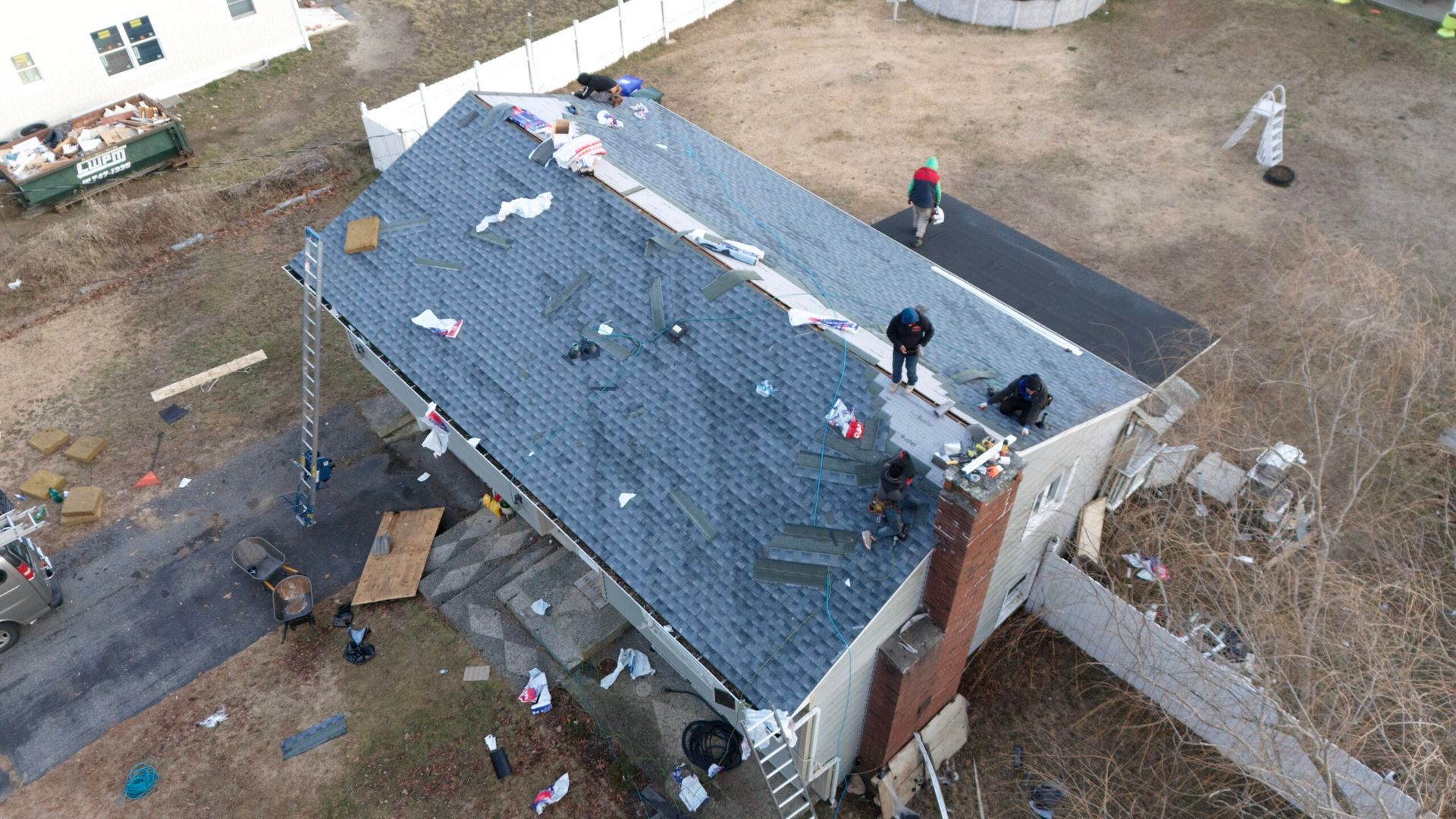 Aerial view of workers repairing a damaged roof on a house with debris around it