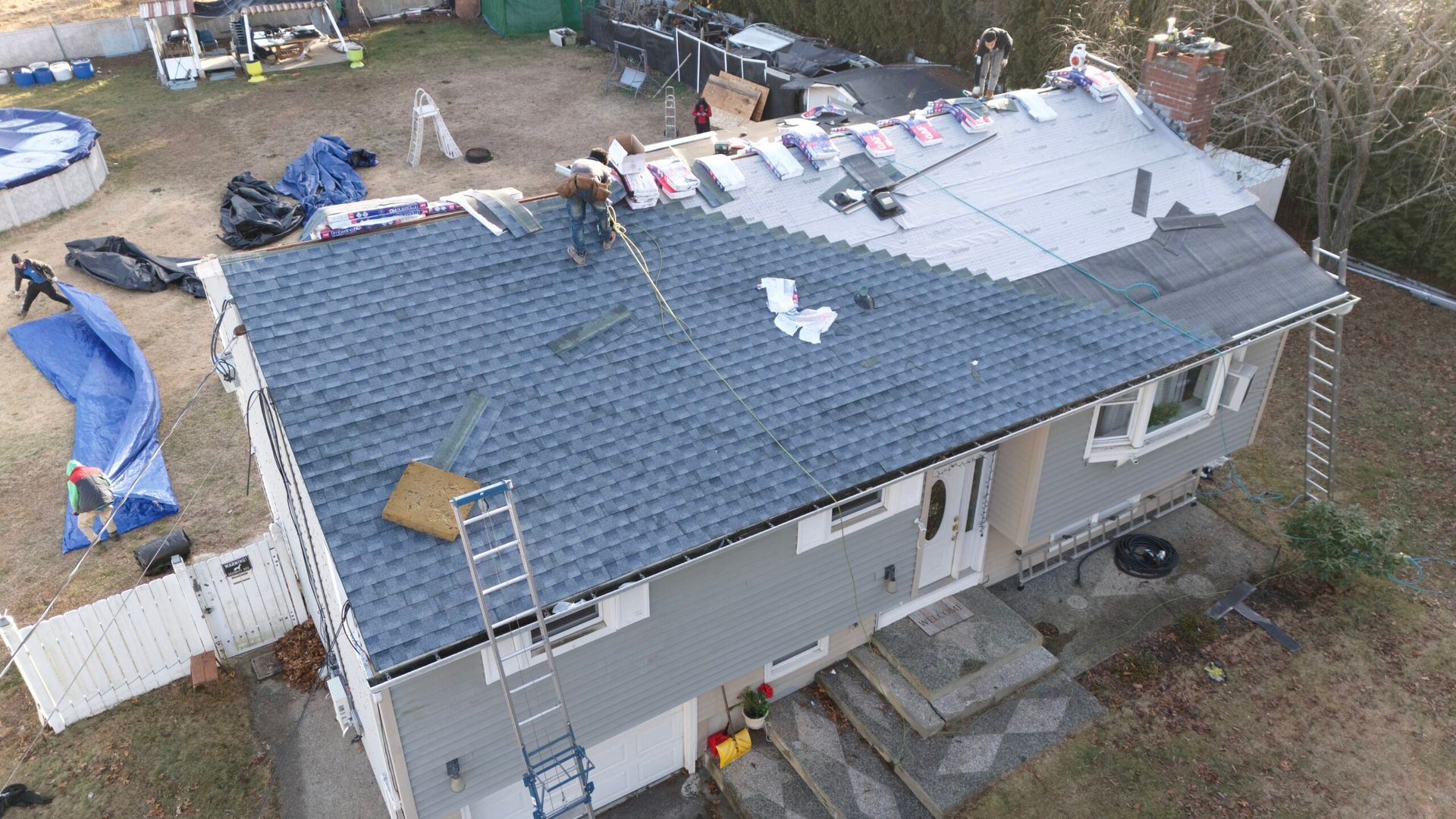 Aerial view of a house with a new gray roof under construction, with tools and materials scattered around
