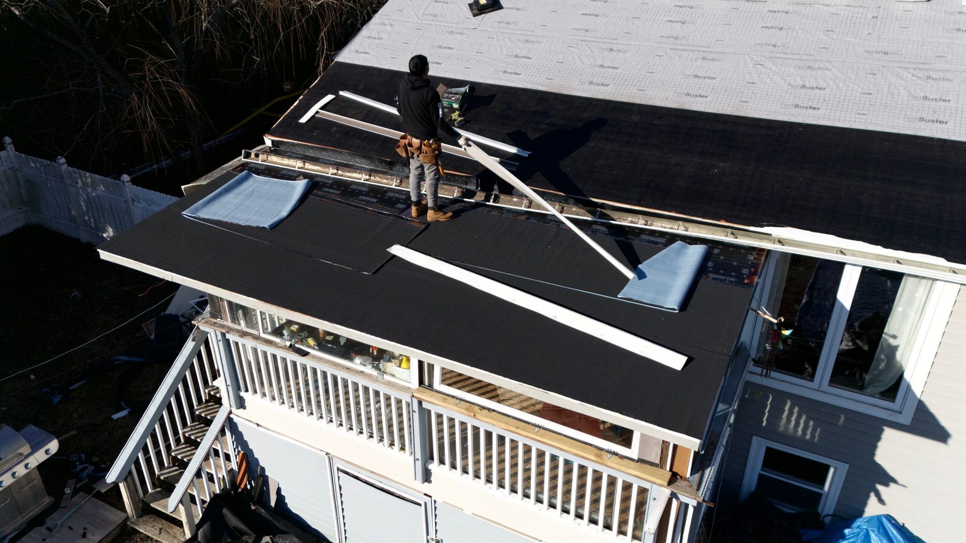 Worker on a rooftop installing black roofing material and skylights on a house under construction