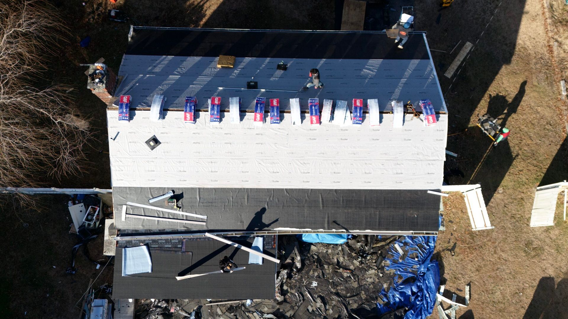 Aerial view of a roof with a row of colorful items along the ridge and scattered construction materials nearby.