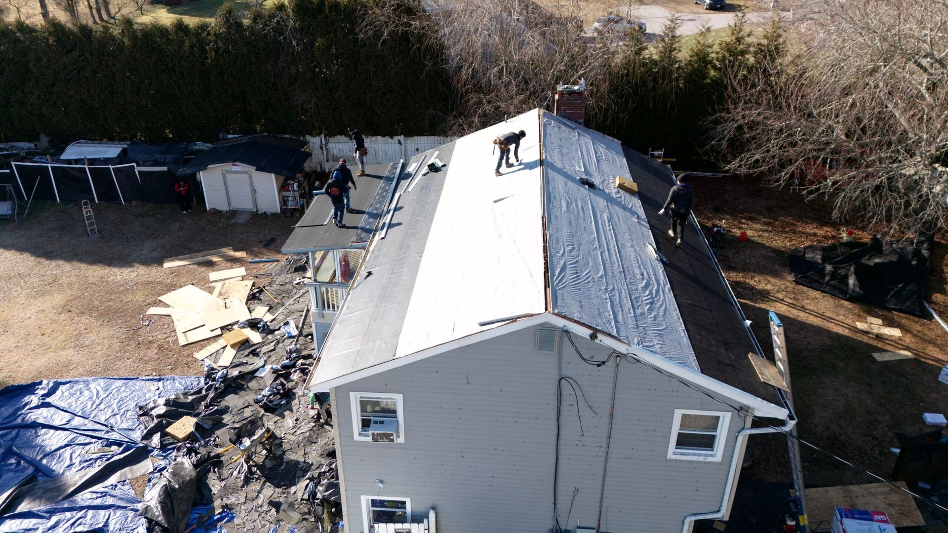 Aerial view of a house with a damaged roof and debris scattered around the yard.