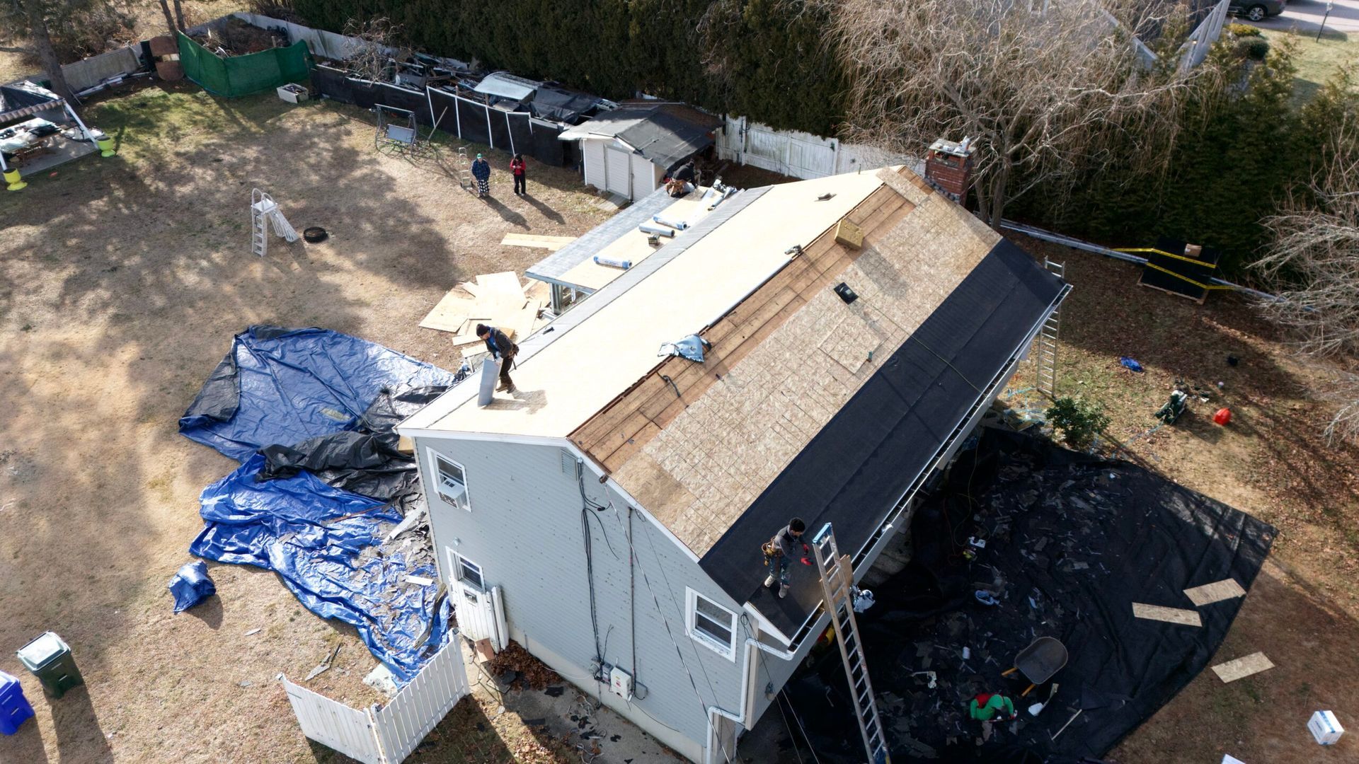 Aerial view of a white house with a damaged roof and blue tarps in the yard.