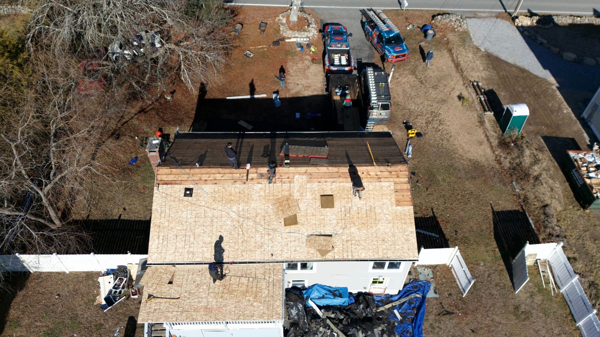 Aerial view of a fire-damaged house with firefighters, trucks, and debris in the yard