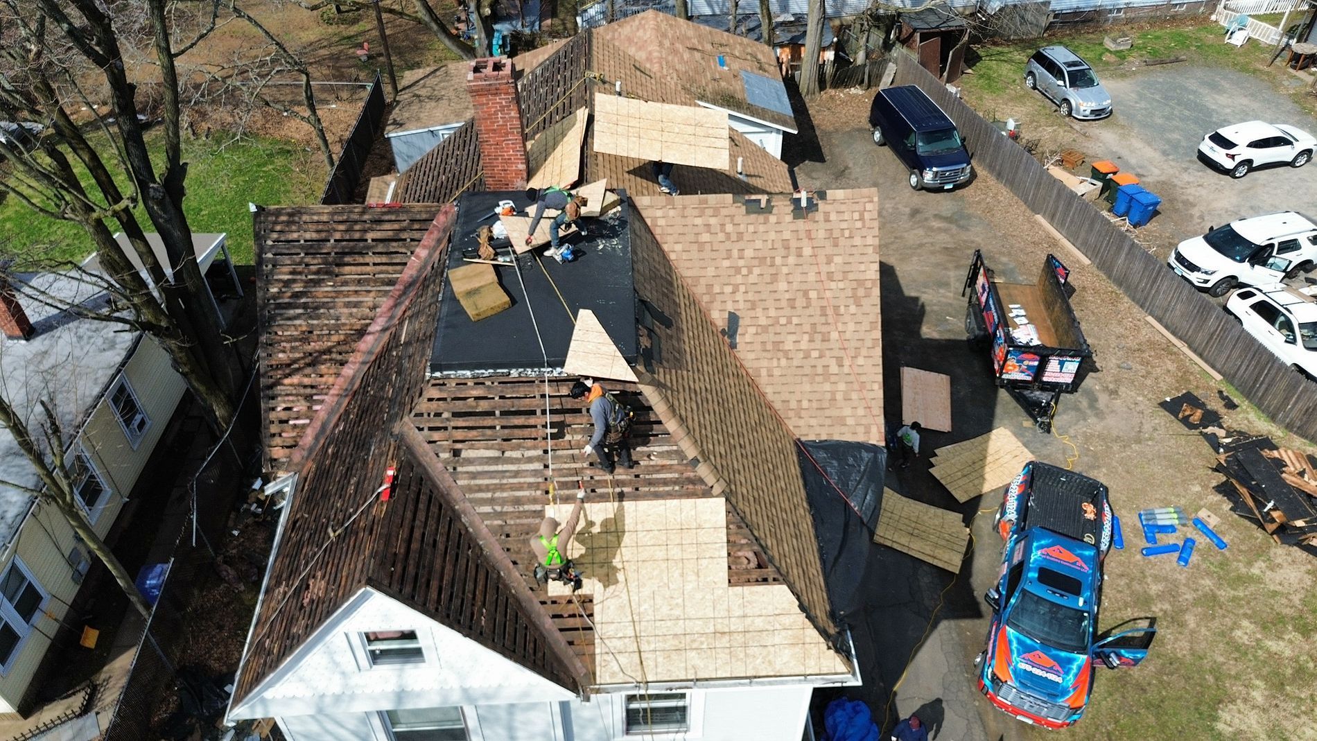 Aerial view of a roof under repair beside a parking area with cars and scattered construction materials.