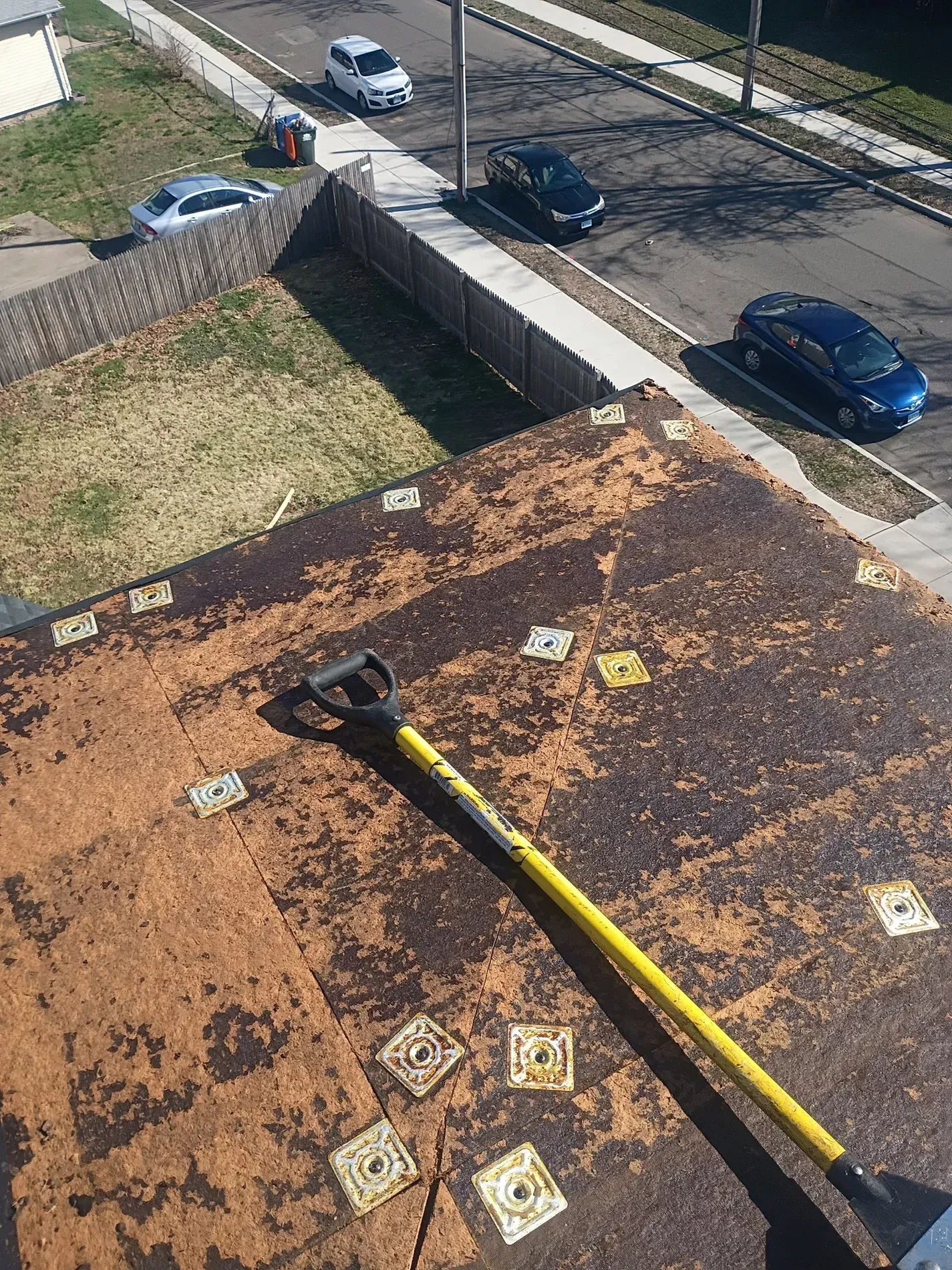 Rooftop with yellow pipe and scattered tiles beside a parking lot and cars below.